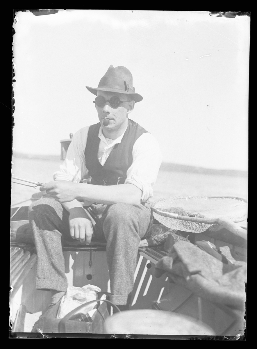 Harald Olsson med solglasögon och pipa sitter i en båt och fiskar.