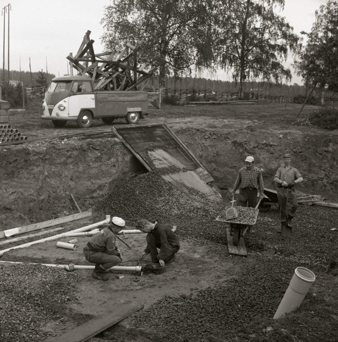 Två män lägger rör i en husgrund och två andra män fyller grunden med grus vid byggnation av bostadshus vid gården Sunnanåker, 1967.