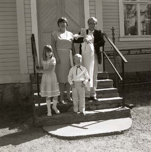 En familj bestående av mor, far och tre barn poserar på en trappa. Det ena barnet bär dopklänning, 1984.
