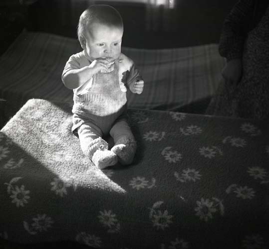 Ett barn sitter på en blommig filt och äter något, 1949.
