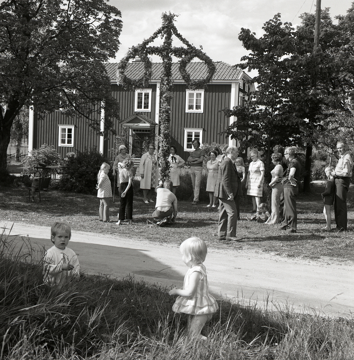En grupp människor dansar runt stången under ett midsommarfirande på gården Sunnanåker, 1972.