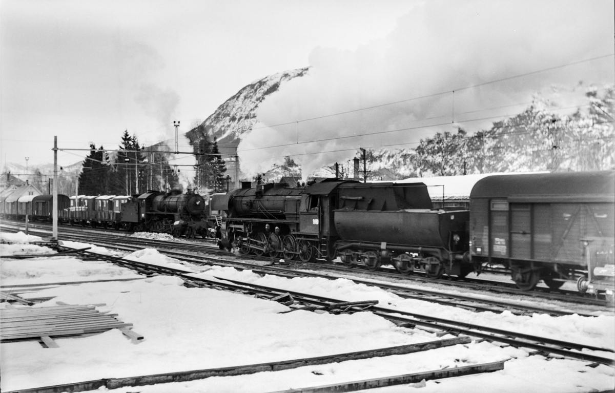 Kryssing mellom østgående og vestgående godstog på Nesbyen stasjon. Togene trekkes av damplokomotiv type 31b nr. 449 og damplokomotiv type 63a nr. 5858.