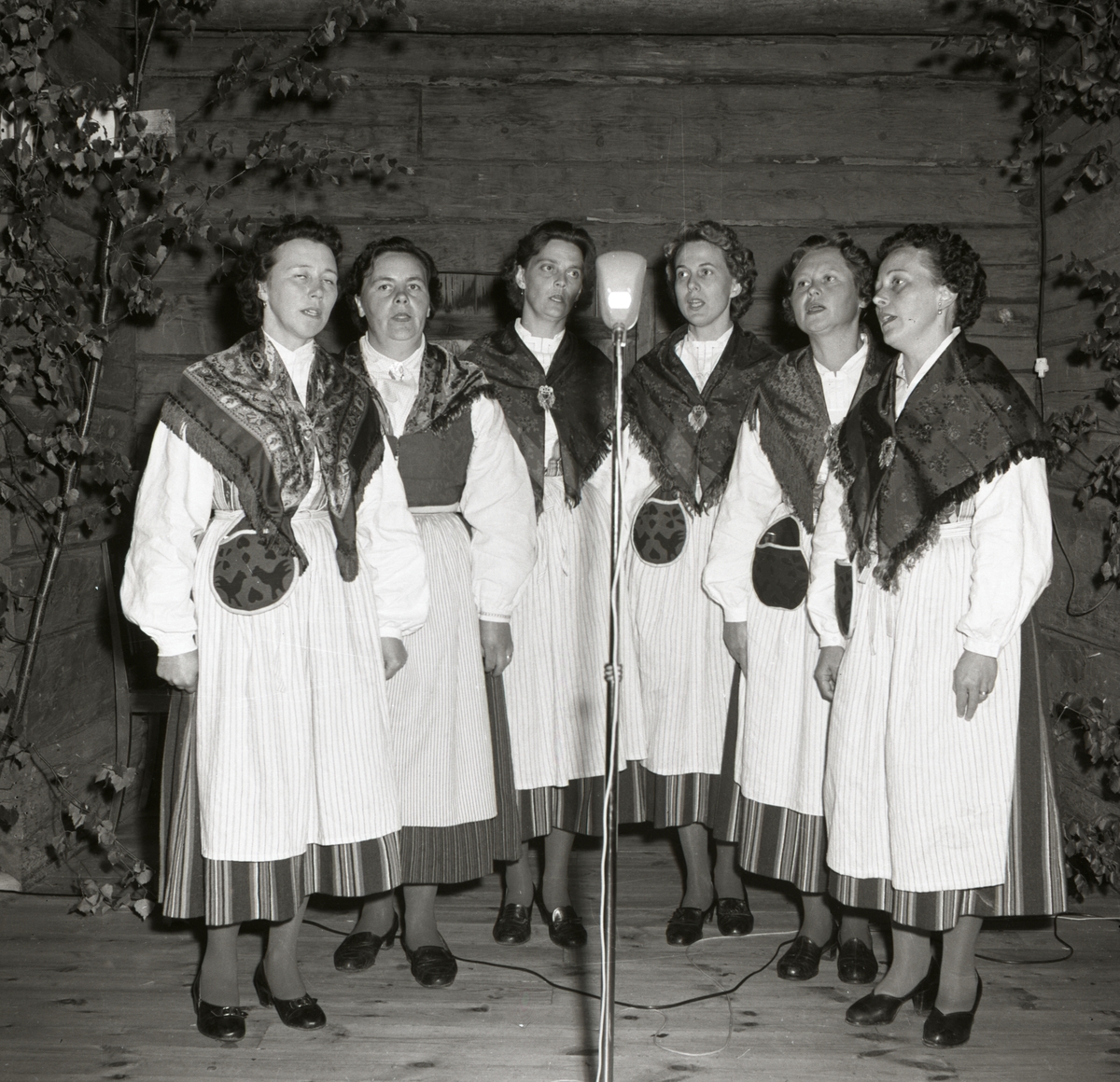 En kör bestående av kvinnor underhåller vid en fest i Rengsjö, 24 augusti 1958. De är klädda i folkdräkter.