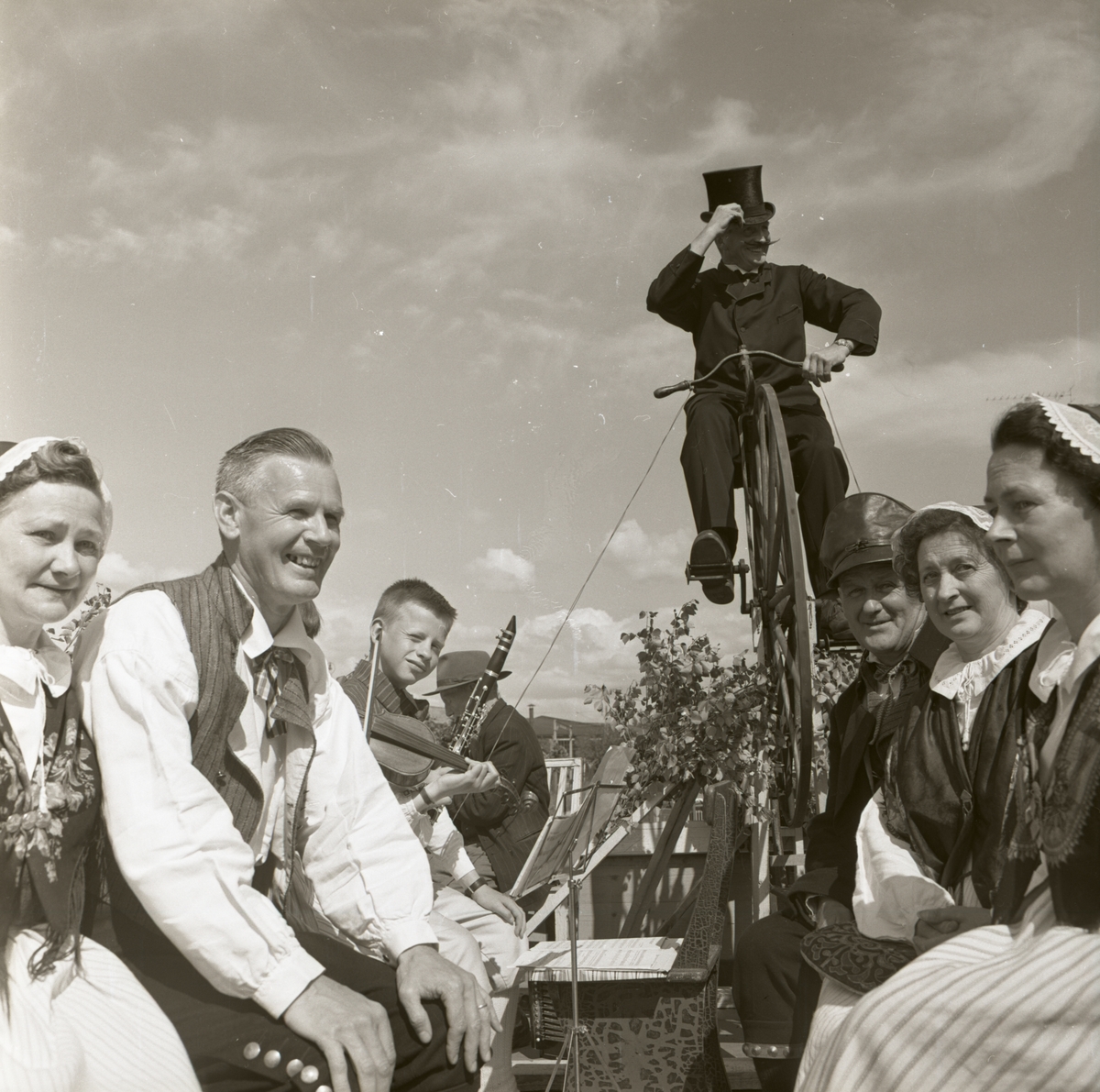 Rengsjö hembygdsförening medverkar vid Bollnäs karnevalen. En man på höghjuling samt människor iförda folkdräkter, 7 augusti 1962.