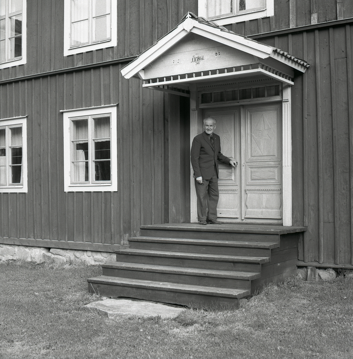 En man står på förstukvisten framför ett timrat huset vid gården Regnells, 1975.