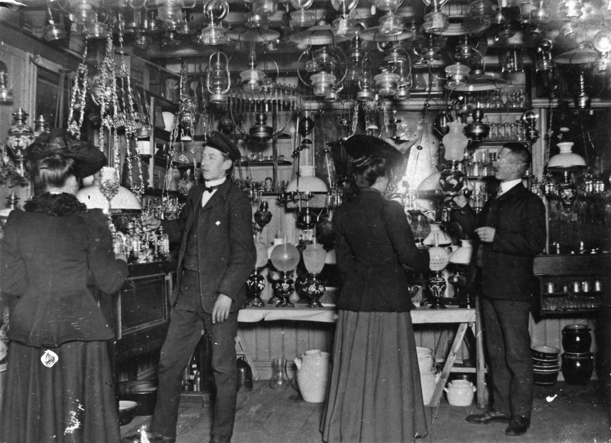 Interiörbild från Alfred Hedéns affär vid Stora Torget. Två män och två kvinnor syns i butiken. Kvinnan till höger är Augusta Karlsdotter som arbetatde som jungfru hos familjen Hedén.