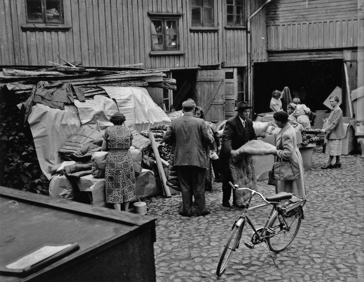 Kvinnor och män inspekterar auktionsföremål under auktion på gården till Tells hus på Kungsgatan 38. I förgrunden en cykel.
Kvarteret Jägaren 11.