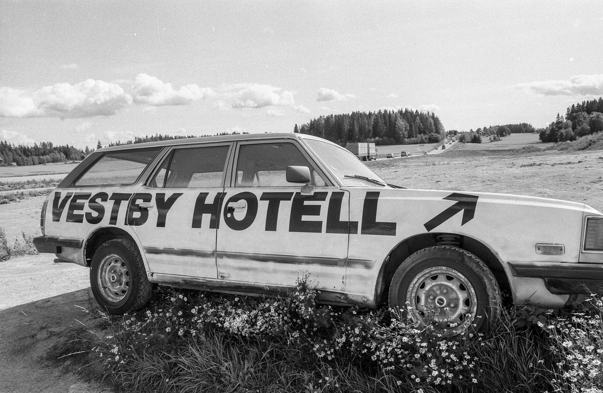 Biler påmalt reklame for Vestby Hotell parkert på et jorde.