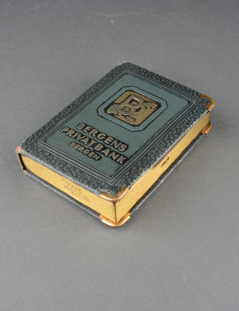 Sparebøsse formet som en innbundet bok med gyldent snitt. Spalte for mynter og sedler på "bokens" topp. Dekor på front.