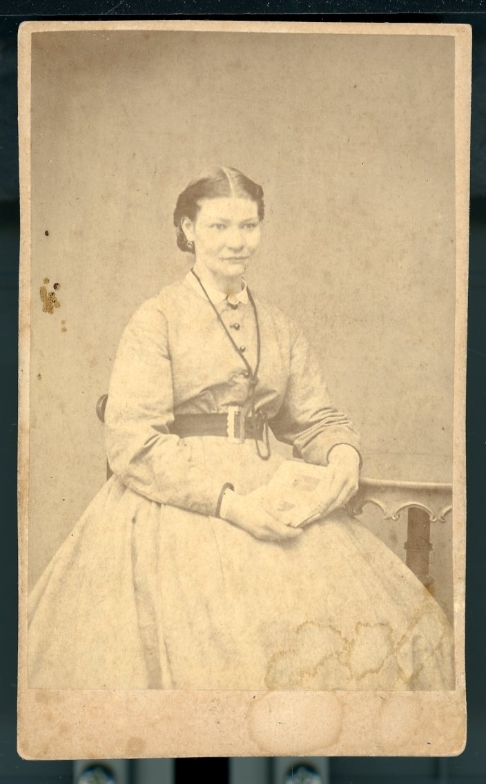 Kabinettsfotograf: Ida Hall med fotoalbum (?) i händerna sittande vid ett bord.