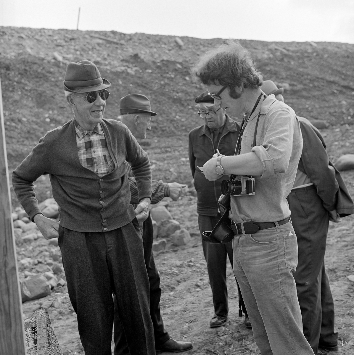 Til høyre på dette bildet ser vi Åsmund Eknæs (1940-1981) på feltarbeid på Fossbakken under garden Nedre Kåterud i Stange, der det tradisjonelle kupefisket etter mort (her kalt «sørenne») i den nedre delen av Svartelva, som på dette tidspunktet var truet av en utvidelse av hovedvegen mellom Oslo og Trondheim, E6-  Eknæs er fotografert med en notatblokk i hendene og kamera på magen mens han snakket med informanten Håkon Berge (1896-1980) fra Stange.

Åsmund Eknæs var fra Krokstadelva i Nedre Eiker i Buskerud.  Han avla magsistergradseksamen i etnologi ved Universitetet i Oslo med avhandlingsarbeidet «Det tradisjonelle laksefiskeriet i Drammenselva - Naturforhold og redskapsutvikling» i 1972  Deretter ble Eknæs ansatt som vitenskapelig assistent ved Norsk Skogbruksmuseum i Elverum.  I 1974 fikk han konservatortittel, etter at en vitenskapelig komité hadde gjennomgått den faglitterære produksjonen hans.  Eknæs var sentral da Norsk Skogbruksmuseum bygde basisutstillinger om ferskvannsfiske, jaktvåpen og tollekniver, og han var en flittig feltarbeider, særlig på steder der det pågikk fiskeaktiviteter.  I 1979 gav han ut boka «Innlandsfiske», som gir en oversikt over innlandsfiskets historie her til lands.  Han foreleste også for grunnfagsstudentene i etnologi om dette emnet.  Eknæs ble dessverre rammet av kreft og døde i 1981, bare drøyt 40 år gammel.