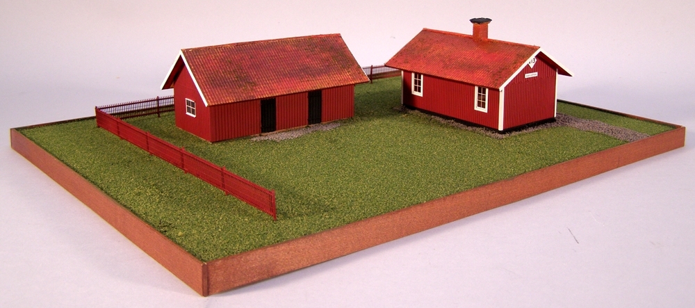 Modell av Banvaktstuga 213 Hosäter med uthus och staket,  i skala 1:87 H0. Husen är byggda av etsark i mässing och målade med modellfärg av märket "Model master". Basplatta av Mdf med strömaterial.
