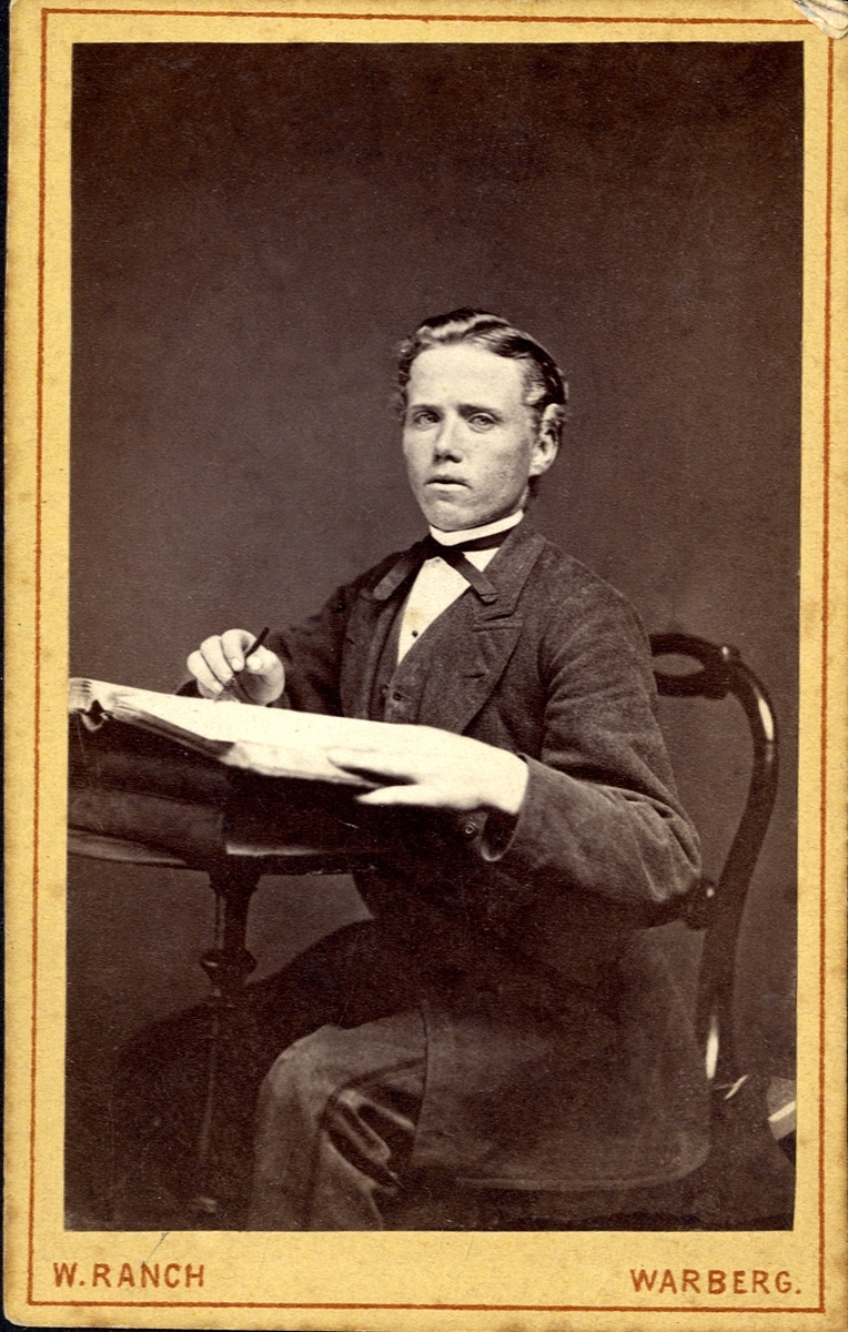Porträtt (knäbild, halvprofil) av en okänd ung man klädd i kostym och stärkkrage med fluga, 
som sitter vid ett bord med en uppslagen bok. 

Bildtext: (baksida) W. Ranch, Fotografisk Atelier, Warberg.