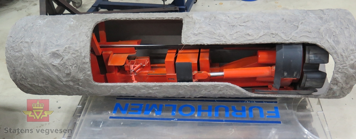 Minityrmaskin i et gjennomskåret rør, som forestiller maskinen i bruk i en tunnel.