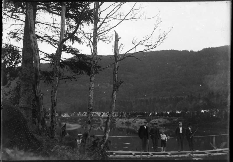 Provisorisk bro over Skjerva. Flere voksne og barn på brua. Militærteltene skimtes i bakgrunnen under åsen.