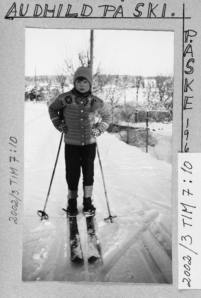 Audhild Håland g. Birkeland (20.7.1951 - ) på ski utanfor heimen på Oshei. Biletet er teke mot nord og idrettshallen ligg nå (2003) til høgre i bakgrunnen.
Same som 2002.3TIM.7.010 med tekst omkring frå album.