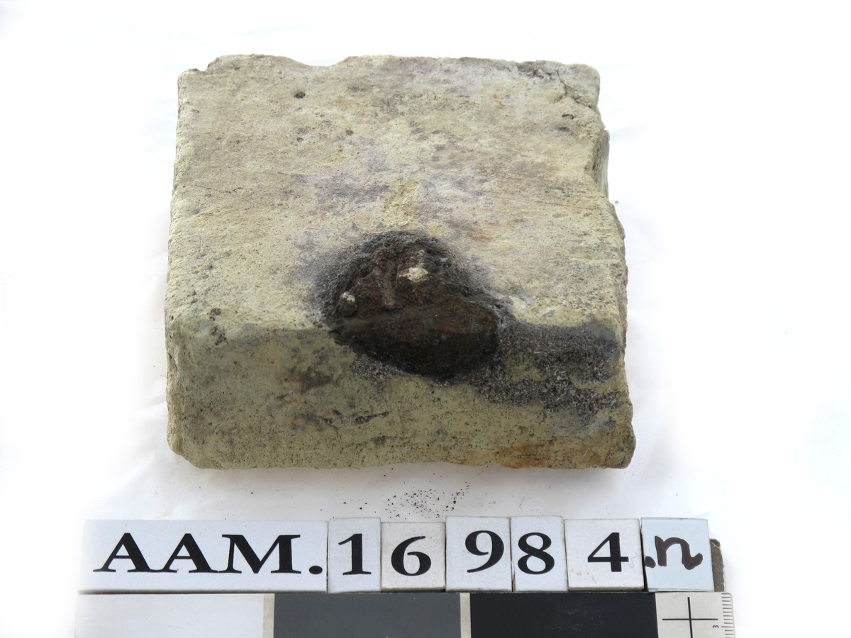 Teglstein fra slaveskipet "Fredensborg. Tilnærmet halv stein, med et stort sort hull på en kant.