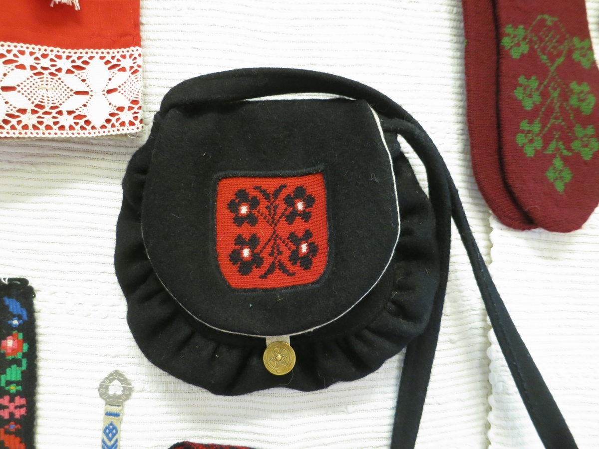 Väska nytillverkad i svart kläde. Flerfärgsvirkad detalj i rött, svart och vitt ullgarn i locket. Mässingknapp som lås.