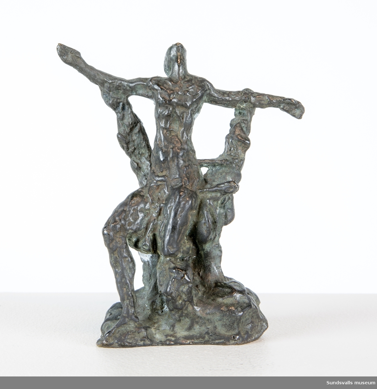 En skulptur i form av en stående man lutad emot en träliknande konstruktion med huvudet kraftigt böjt bakåt.