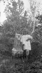 Portrett av liten pike stående utendørs med gyngestol.