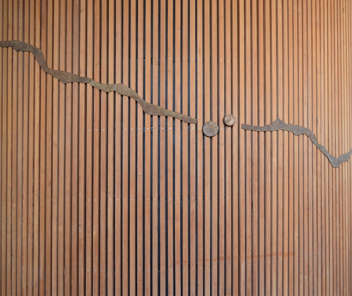 Kunstverket består av bronseelementer som er felt inn i veggen i to etasjer. Motivene er avstøpninger av bølgepapp og sandblåste tverrsnitt av trestammer.  Arbeidet inngår i en utsmykning som omfatter to deler, en utendørs og en innendørs.
