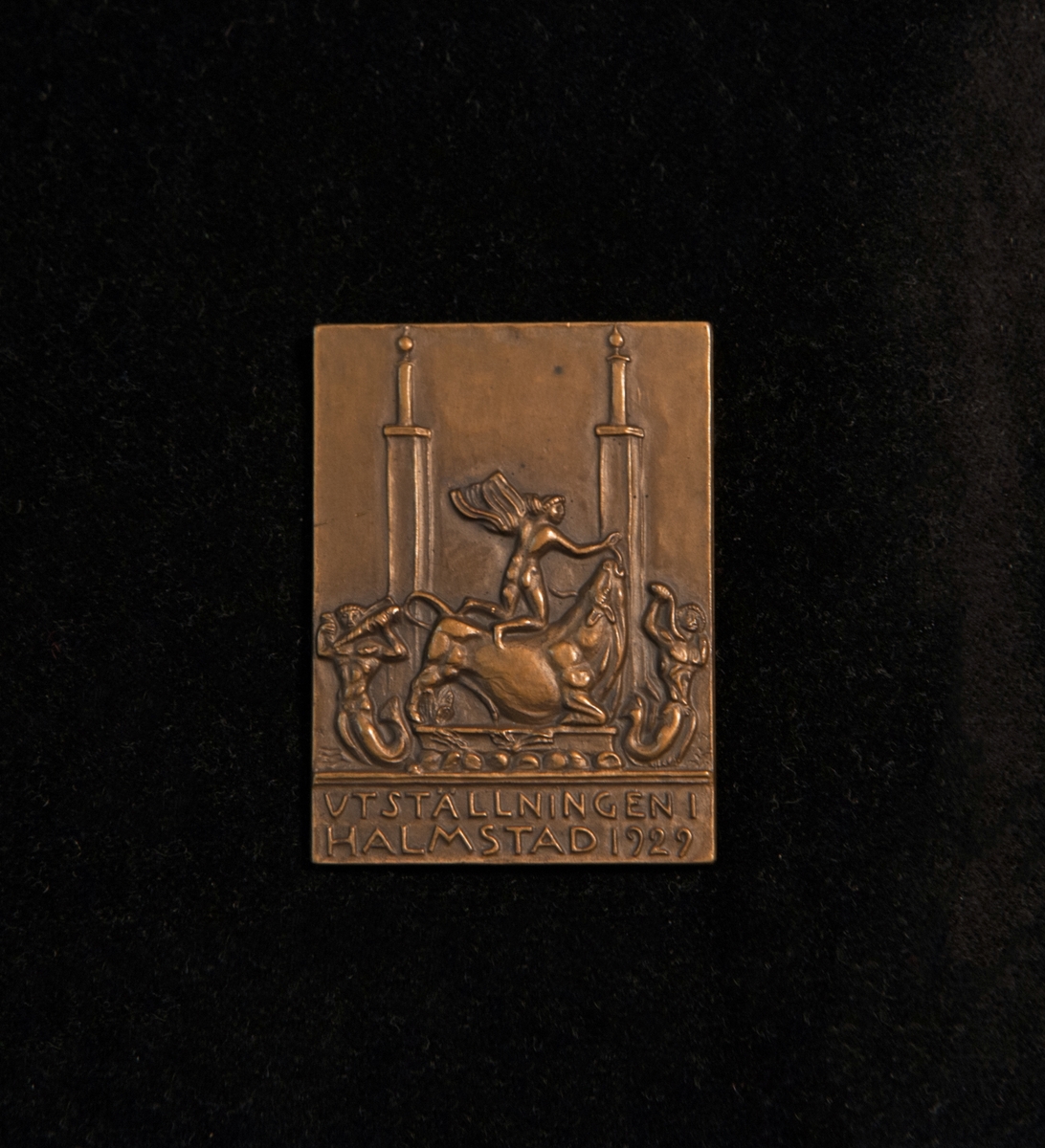 Plakett i brons. Åtsida: Bild av tre mansgestalter och en tjur. Text "Utställningen i Halmstad 1929". Frånsida: Graverad logotype "Löfsko".