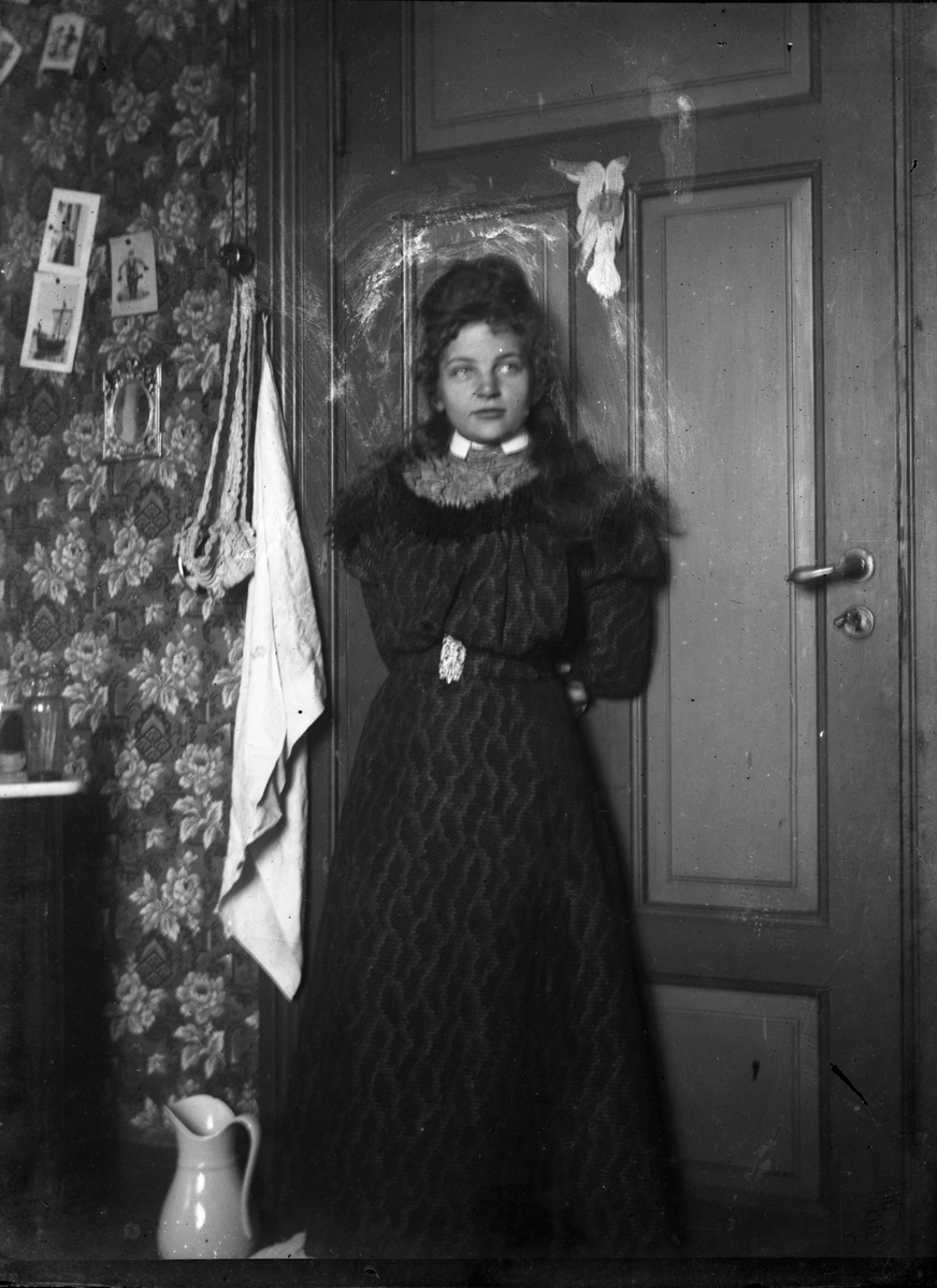 Portrett av ung kvinne i enkelt interiør, kledd i 1890-talls kjole

Antatt fotosamling etter Anders Johnsen