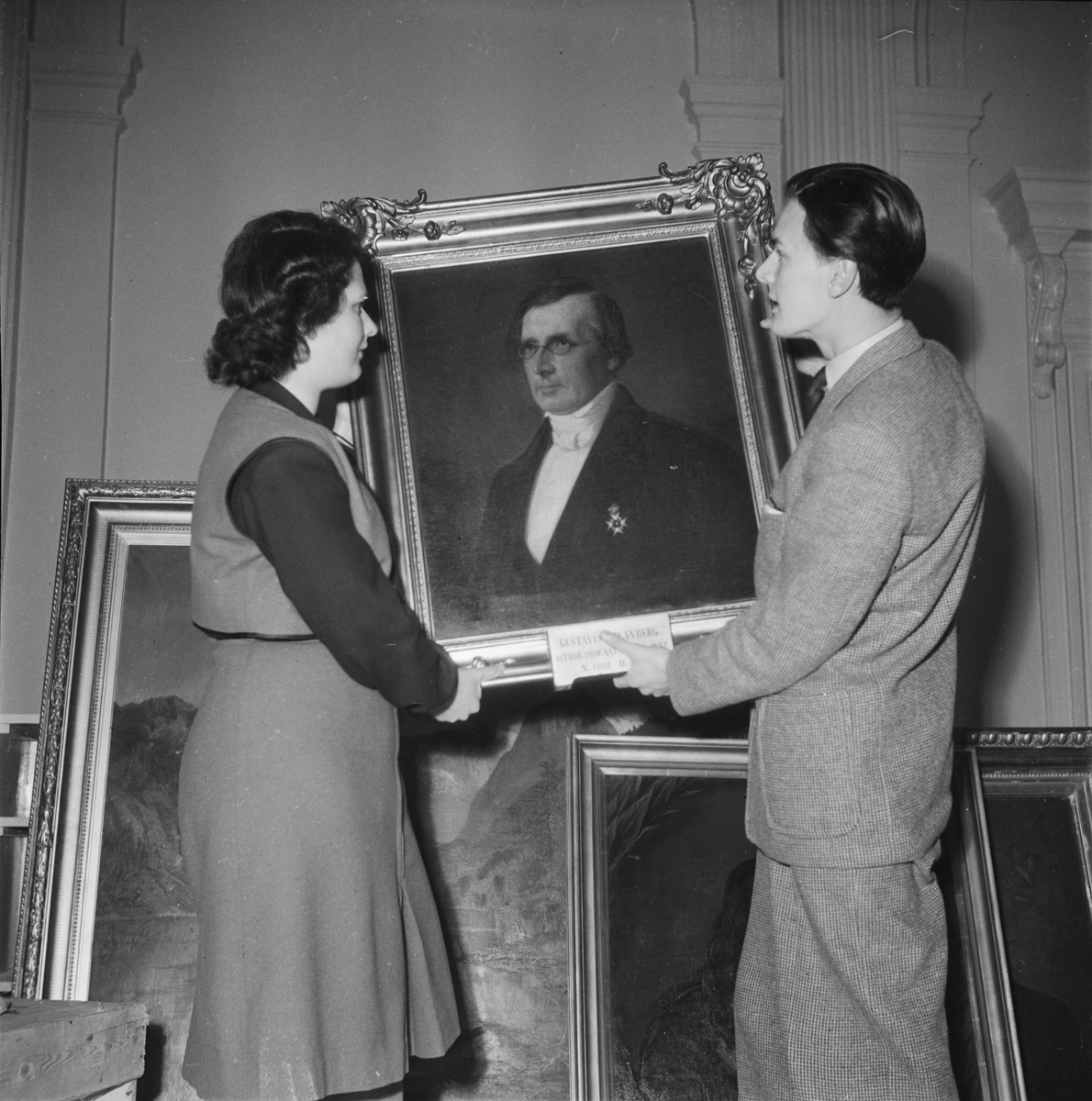 En kvinna och en man håller i en porträttmålning, restaurering inför Östgöta nations 300-årsjubileum, Uppsala 1946