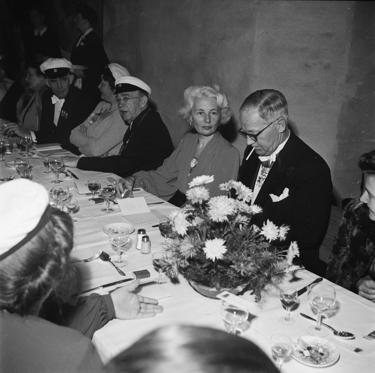 Män och kvinnor i studentmössor vid dukat festbord, sannolikt på rikssalsbanketten i samband med Östgöta nations 300-årsjubileum, Uppsala 1946