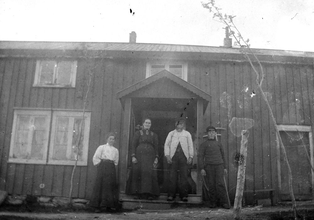 Leirfjord. Fire personer foran inngangspartiet ved huset.