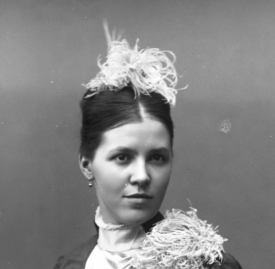 Porträtt av Mathilda Ranch, sittande i elegant klänning, vita handskar samt hår- och axeldekor.
(Se även MR2_2459 och MR3_2600)