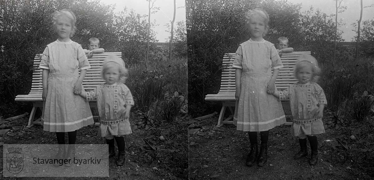 Borghild og Christian Eckhoff i hagen. Bak benken står en gutt og lurer...Stereofotografi..