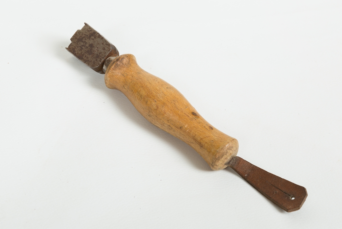 En snittkoliss med dreid skaft i et lyst og lakkert treverk med lærhempe. Snittkolissen anvendes til å pusse sålekanten med.