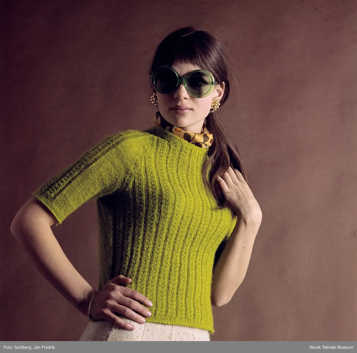 Kvinnelig modell med en grønn mønstret strikket topp med halvlange ermer.