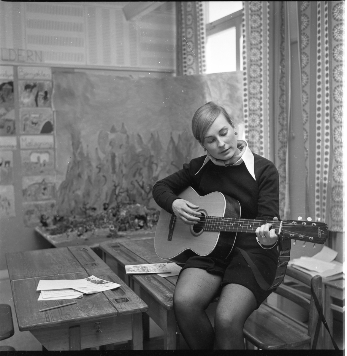 Lärarinnan Marietta Juhlin sitter på kanten av en skolbänk och spelar gitarr. På Ribbaskolan i Gränna.
