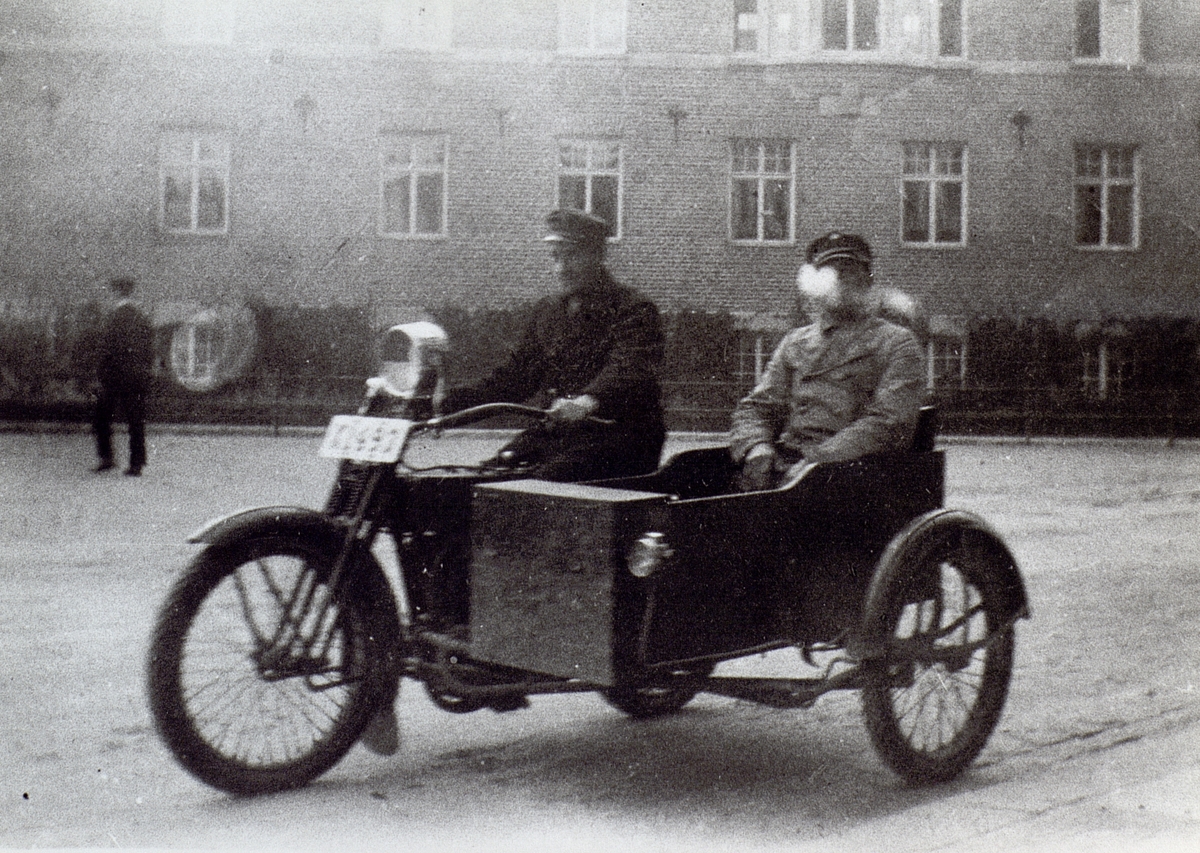 Fotot är taget utanför Sundsvallsbankens hus, efter Hamngatan, Hudiksvall. Karl Kristmansson kör motorcykel med sidovagn. Motorcykel är av modellen X1493 Harley Davidson 1924 1000cc 20 hk. Registrerad den 6/5 1924 på Telegrafverket Gävle - Hudiksvall.