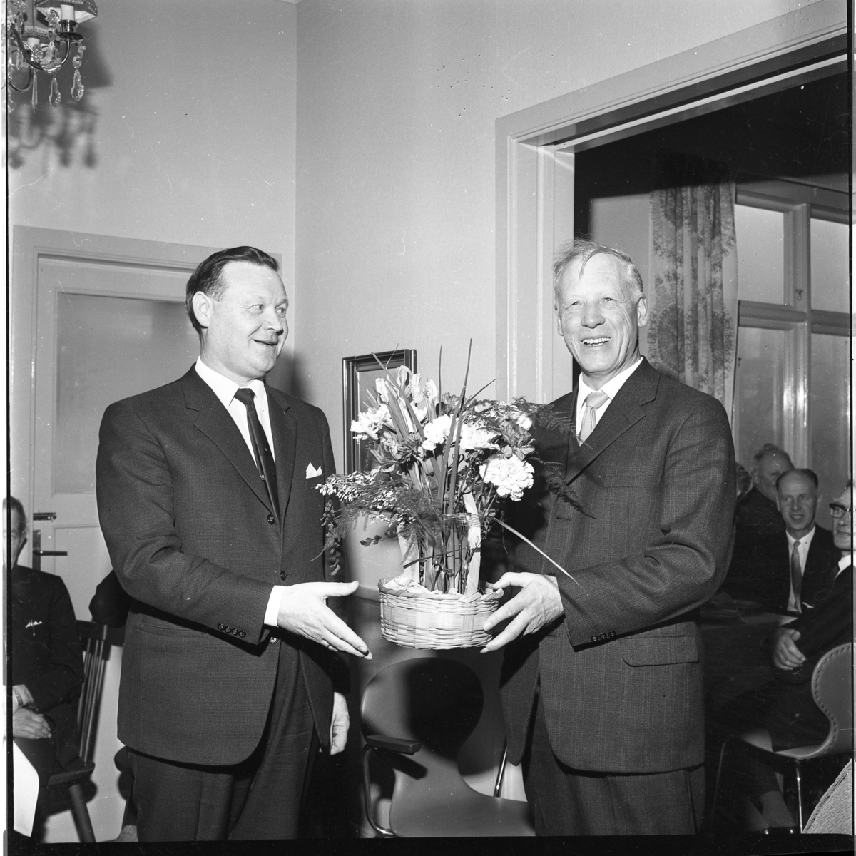 En okänd och Erland Skoog till höger håller en blomma i en korg mellan sig. Det är är Gränna Biodlarförenings 50-årsjubileum på Örensbaden. Skoog är dess ordförande.