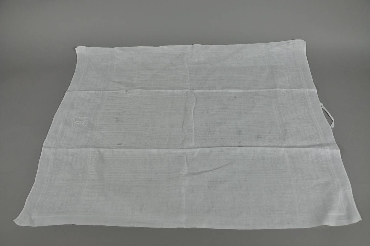 Hvitt håndkle av lin, rektangulær form. Tekstilen er noe slitt.