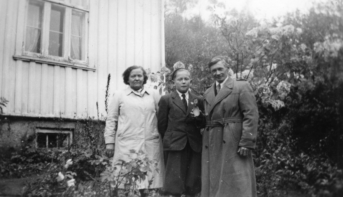 Tre personer oppstilt i en hage med hus i bakgrunnen