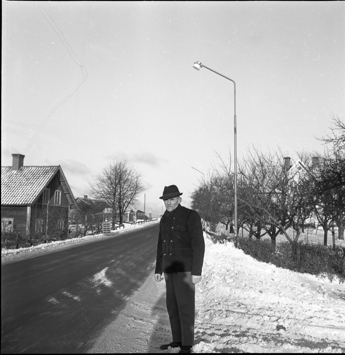 Aldor Jonsson står utmed snökantad väg genom Uppgränna framför ett gatljus. Uppgränna har fått vägbelysning.