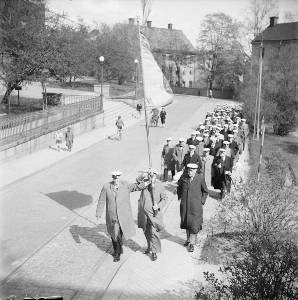 Flera personer iförda studentmössor tågar tillsammans längs Biskopsgatan, Östgöta nations minneslandskap, Uppsala 1949