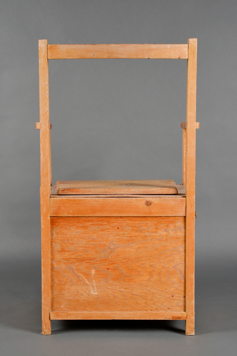 En toalettstol med armlener laget av heltre og kryssfinér. Den har sammenføyninger med skruer og lim samt treforbindelser. Både sete og rygg er firkantet på form. Ryggen består kun av en firkantet ramme. Setet har et lokk som kan tas av. Under lokket er setet med et hull i midten. På venstre side er det en dør med dørknott øverst til høyre. Inni stolen kan man plassere potte eller bøtte. Stolen er lakkert utvendig.