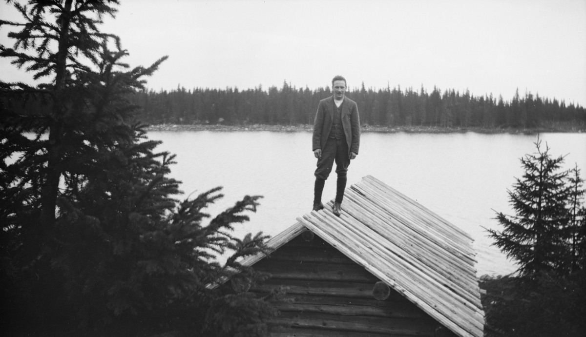Mann stående på taket til ei fiskerbu eller et båtnaust