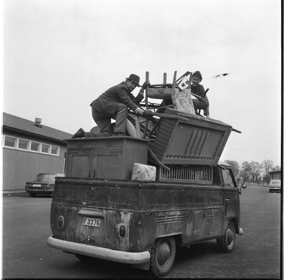 En Volkswagen pickup fullt lastad med olika möbler och högst upp två män som packar. De står möjligen på Ribbaskolans gård.