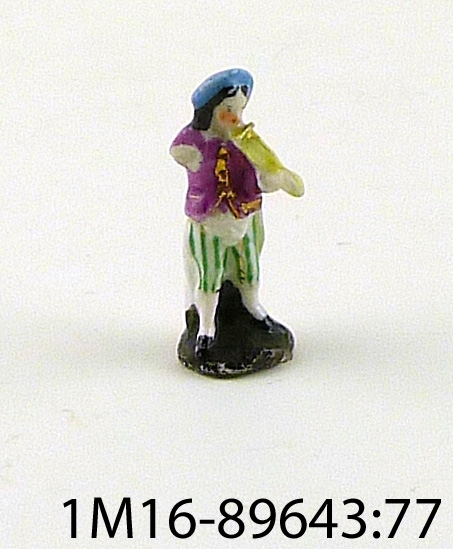 Leksak eller figurin föreställande man i kläder i lila, grön, blå, gul, grön och guld.