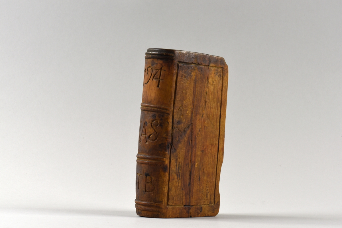 Fodral till psalmbok i trä. Fodralet är utformat som en bok där en sida är försedd med ett skjutlock. På ryggen inristat årtal samt initialer.