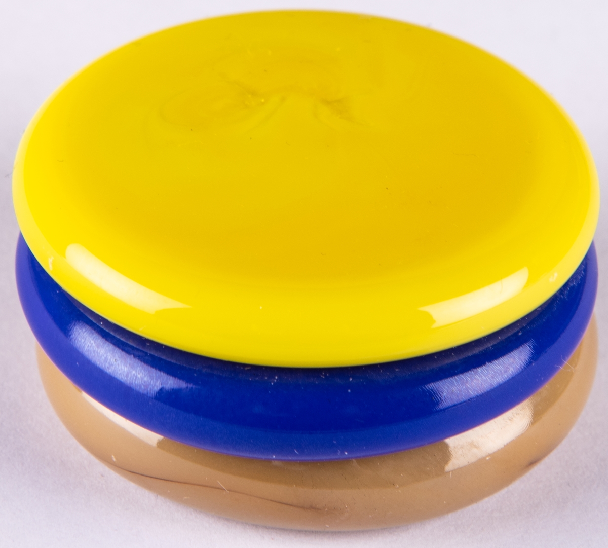 Brevpress, "Småkaka" i kristall. Uppbyggd av tre cirkelrunda hopfästa plattor i beige, blått och gult.