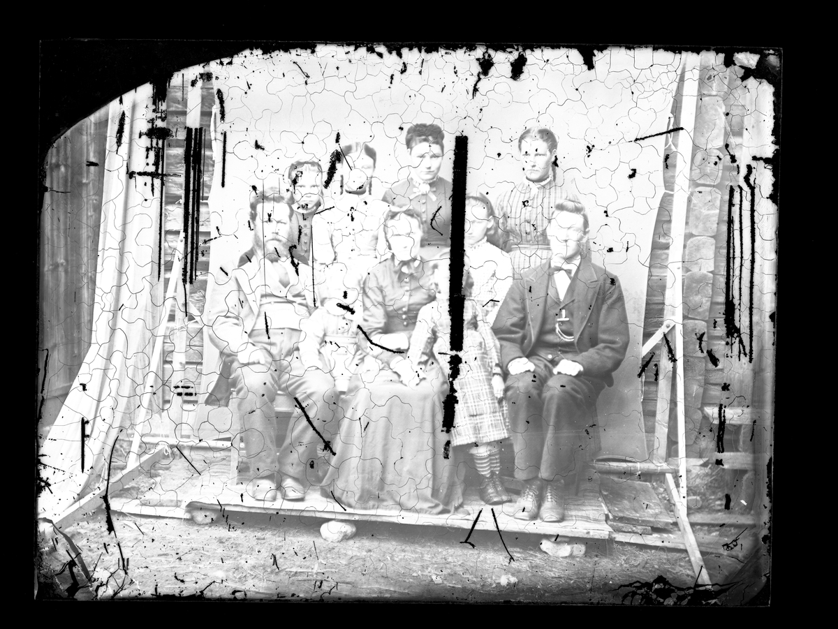 Fotosamling etter fotograf Knut Aslaksen Berdal. f. 1829 Einlaugdalen Vinje, d. 21.01.1895. Familieportrett av gruppe på 10. Mannen med skjegg til venstre, er ant. Halvor Tarjeison Grønlid (1850-1927)