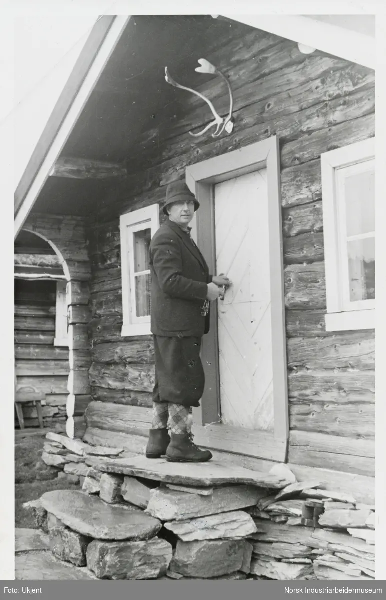 James Coward står på øverste trappetrinn ved inngangsdør til hytte med nøkler i hånden