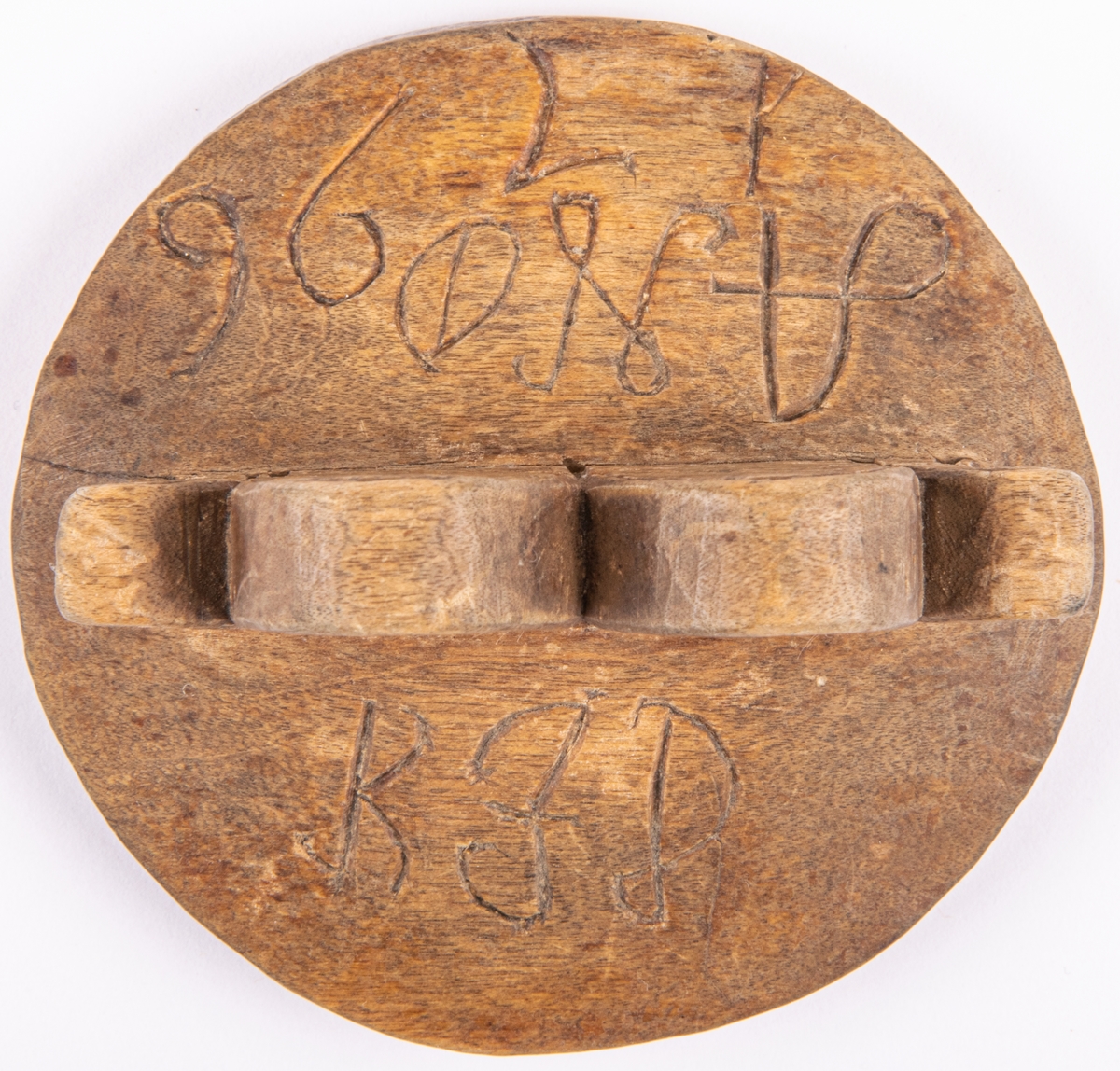 Messmörskrus av trä. Rund skiva med mönstrad stämpelsida, geometriska mönster med uddsnitt och karvsnitt. På ovansidan litet handtag som liknar en krona. Märkt BID ANo1796